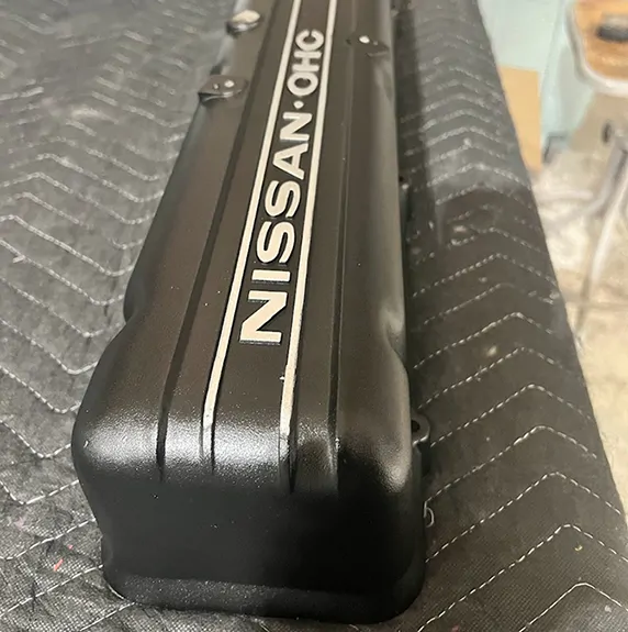 Black Nissan OHC valve cover with silver lettering