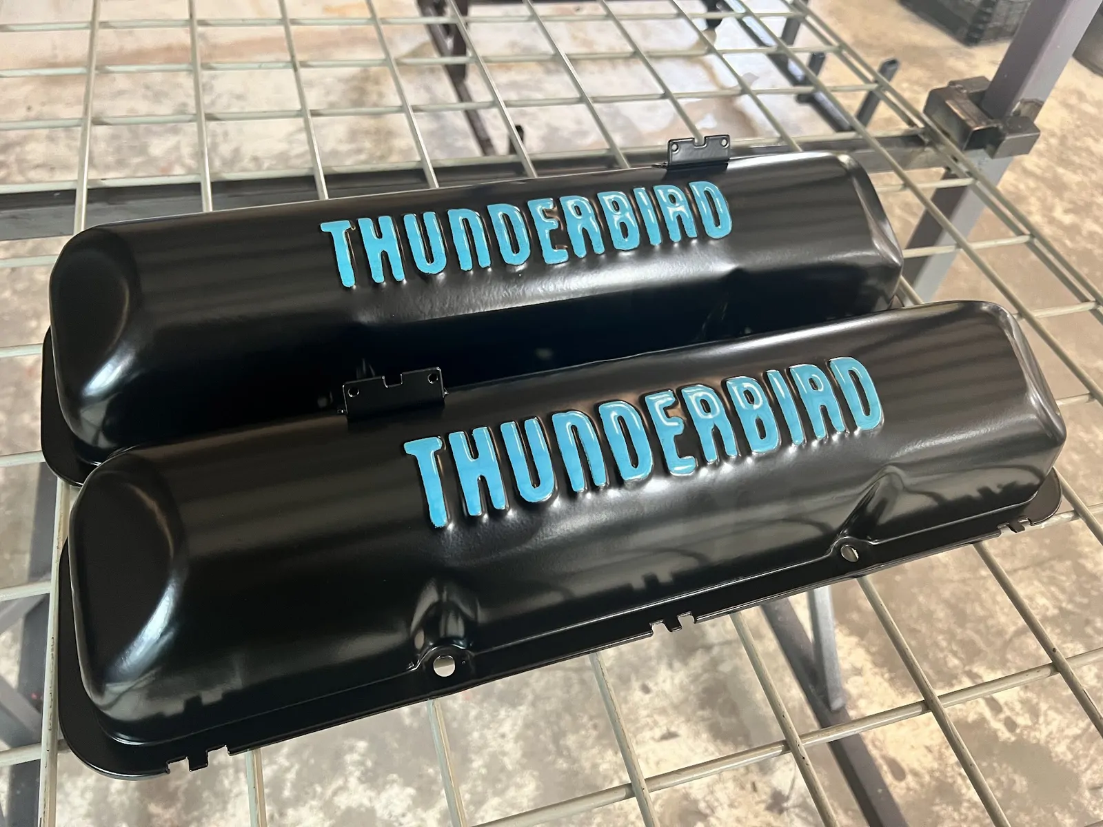 Black Thunderbird valve covers with blue lettering on the drying rack