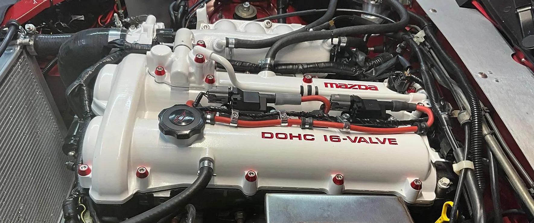 White Mazda DOHC 16-valve cover with red lettering, installed in the engine bay